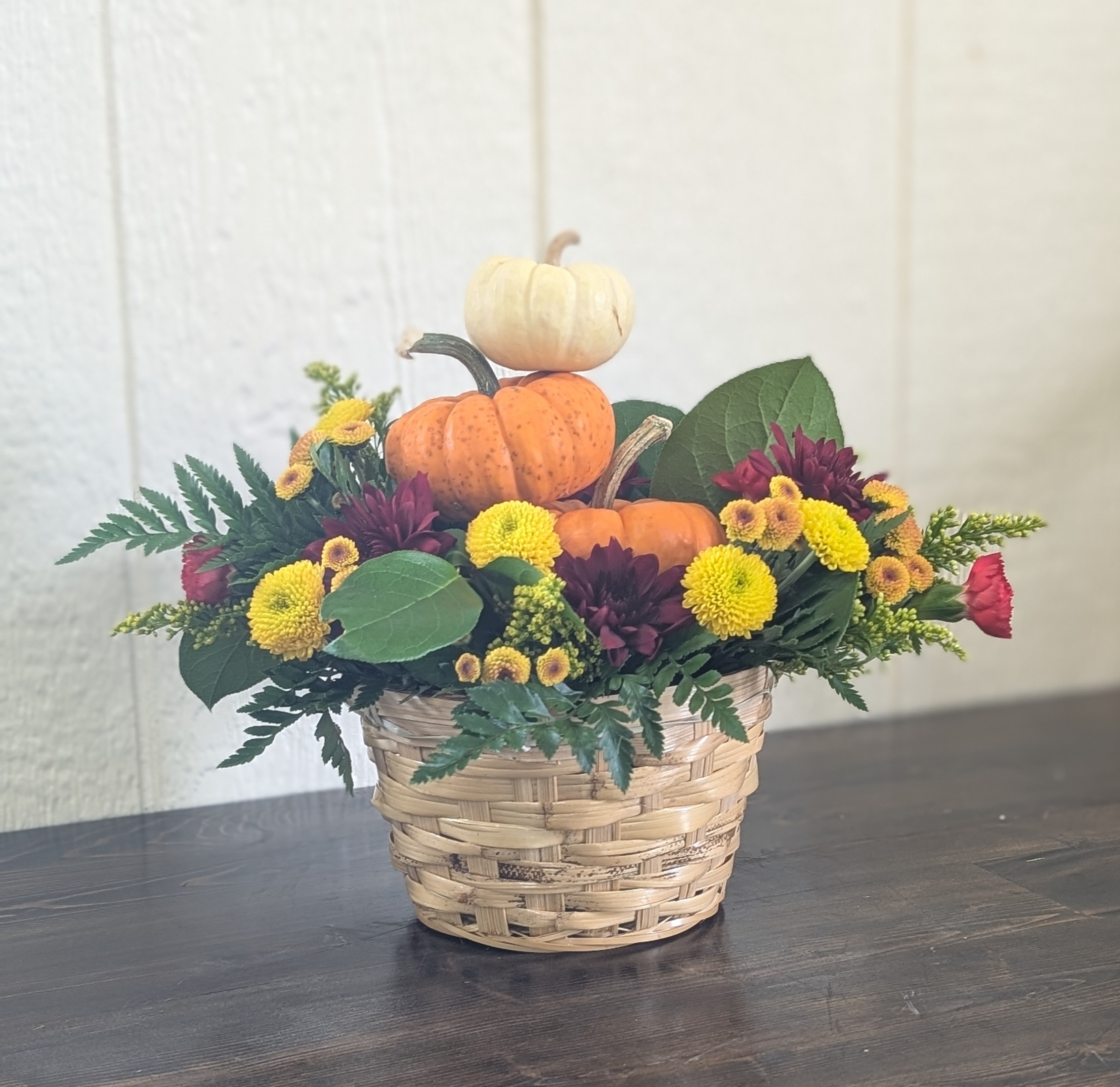 Basket of fall flowers with mini pumpkins on a wooden table with a white background.