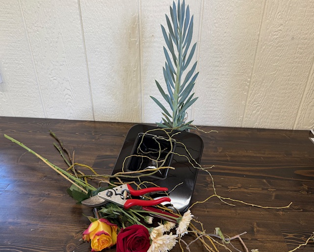 Supplies to create a modern arrangement on a wooden table with a white background.